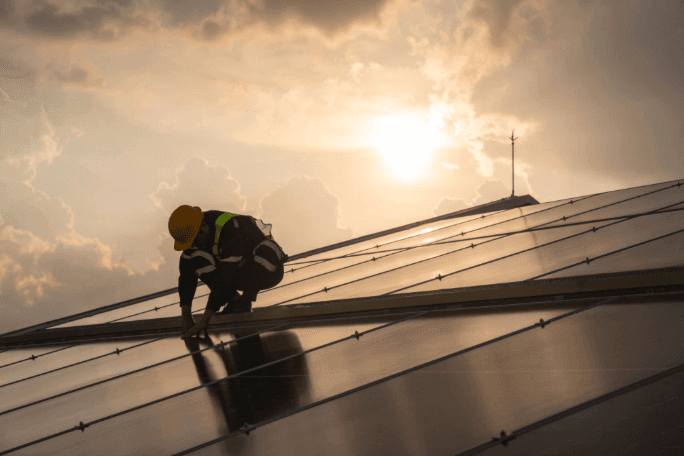 Worker installing solar panels on a residential roof at sunset, representing key considerations for buyers and sellers in solar-equipped home transactions.