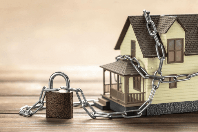 When Your VA Loan Benefit Feels Locked House wrapped in chains and locked with a padlock, symbolizing VA loan entitlement tied up from an existing mortgage