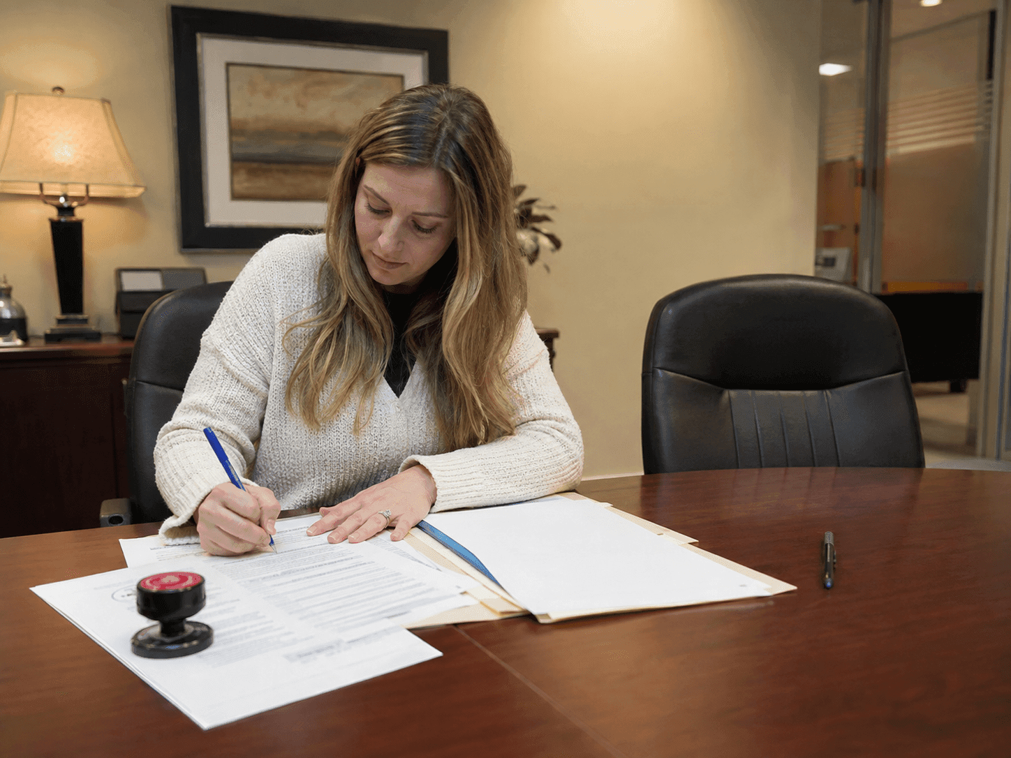 Military spouse signing closing documents at a title company table beside an empty chair.